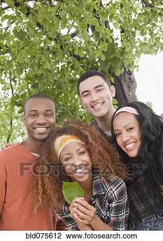 Stock Image - Friends holding leaf under tree. Fotosearch
