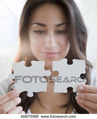 Stock Image - Hispanic woman holding two puzzle pieces. Fotosearch