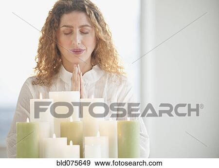 Stock Photo - Hispanic woman praying by candles. Fotosearch