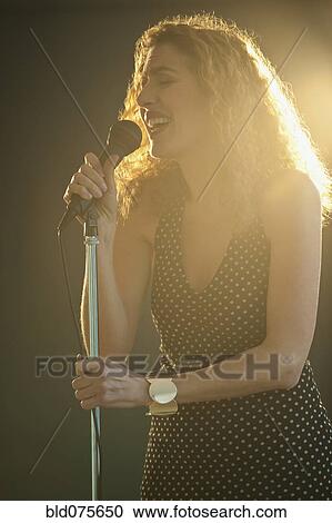 Stock Image - Hispanic woman singing into microphone onstage. Fotosearch