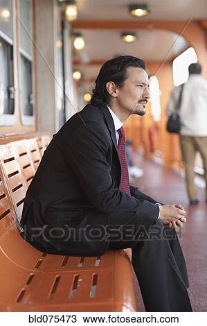 Stock Image - Mixed race businessman on bench and looking pensive. Fotosearch