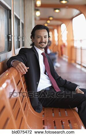 Stock Image - Mixed race businessman smiling on bench. Fotosearch
