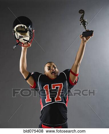 Mixed race football player holding helmet and trophy overhead View Large Photo Image Stock Photo - Mixed race football player holding helmet and trophy overhead. Fotosearch