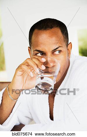 Picture - Mixed race man in bathrobe drinking water. Fotosearch