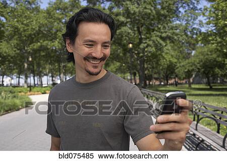 Stock Photography - Mixed race man looking down at cell phone in park. Fotosearch