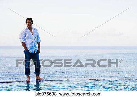 Stock Photo - Mixed race man standing on edge of infinity pool. Fotosearch