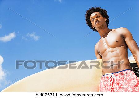 Serious African man holding surfboard View Large Photo Image Stock Image - Serious African man holding surfboard. Fotosearch