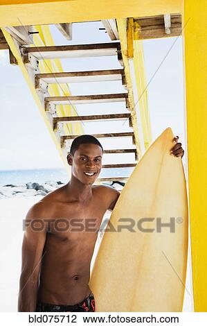 Smiling African man holding surfboard View Large Photo Image Stock Image - Smiling African man holding surfboard. Fotosearch