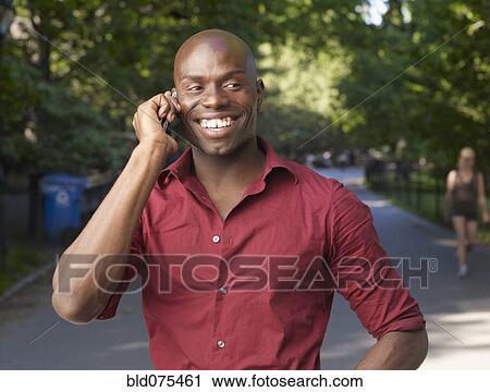 Stock Image - Smiling African man using cell phone. Fotosearch