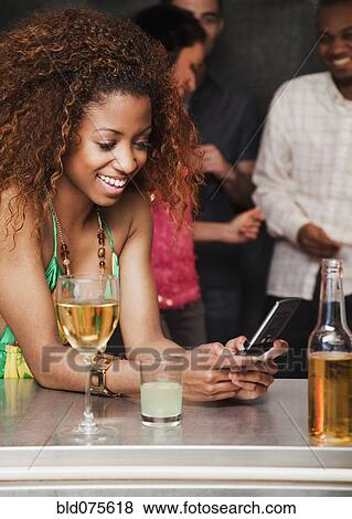 Stock Photo - Woman text messaging at bar. Fotosearch