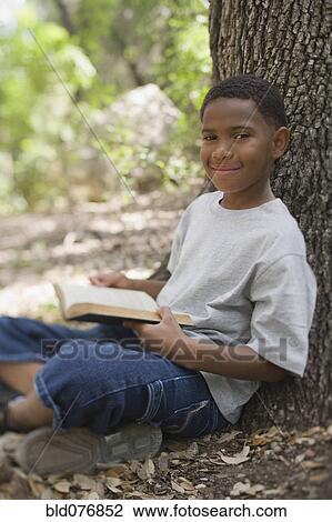 African boy reading book against tree View Large Photo Image Stock Image - African boy reading book against tree. Fotosearch