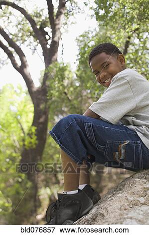 Stock Photo - African boy sitting on rock in park. Fotosearch