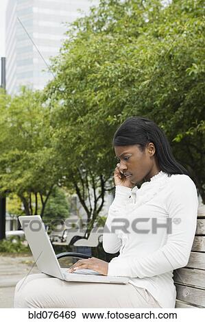 African businesswoman using laptop on bench in city View Large Photo Image Stock Photo - African businesswoman using laptop on bench in city. Fotosearch