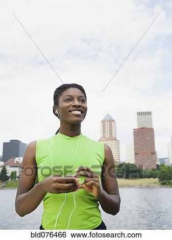 African woman listening to headphones with city in background View Large Photo Image Stock Photograph - African woman listening to headphones with city in background. Fotosearch