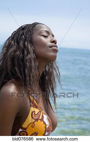 Stock Photograph - African woman relaxing with eyes closed on beach. Fotosearch