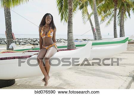 Stock Image - African woman sitting on boat on beach. Fotosearch