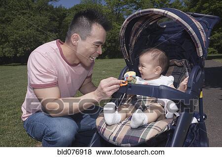 Stock Photo - Chinese father and baby in stroller at park. Fotosearch