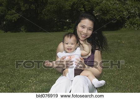 Stock Photo - Chinese mother holding baby in park. Fotosearch