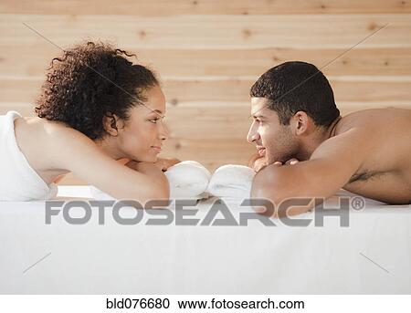 Stock Image - Couple laying face to face on massage table. Fotosearch
