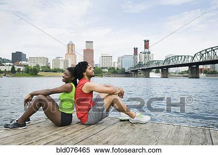 Couple sitting on urban boardwalk along river View Large Photo Image Stock Photography - Couple sitting on urban boardwalk along river. Fotosearch