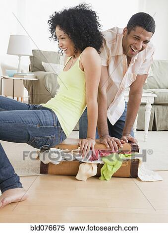 Couple stuffing clothes in small suitcase View Large Photo Image Stock Photography - Couple stuffing clothes in small suitcase. Fotosearch