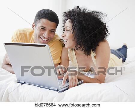 Picture - Couple using laptop on bed. Fotosearch