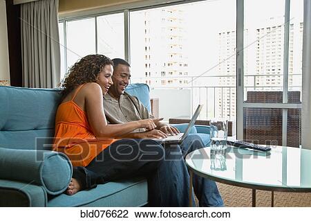 Stock Image - Couple using laptop on sofa. Fotosearch