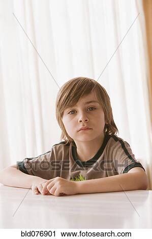 Stock Image - Hispanic boy sitting at table and looking serious. Fotosearch