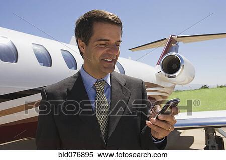 Hispanic businessman text messaging next to private jet View Large Photo Image Stock Photography - Hispanic businessman text messaging next to private jet. Fotosearch