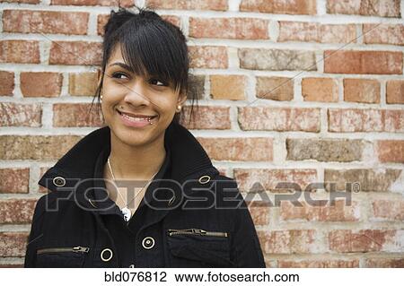 Stock Image - Hispanic teenage girl smiling against brick wall. Fotosearch