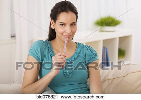 Stock Image - Hispanic woman holding pen on sofa. Fotosearch