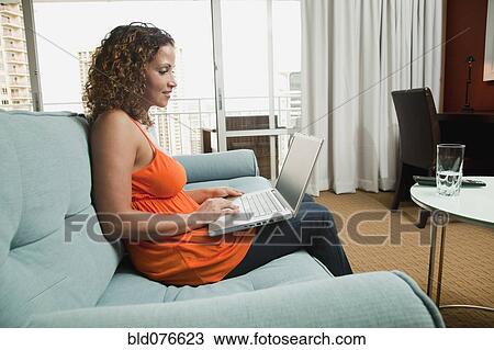 Stock Image - Hispanic woman using laptop on sofa. Fotosearch