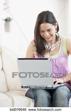 Stock Photograph - Hispanic woman using laptop on sofa. Fotosearch