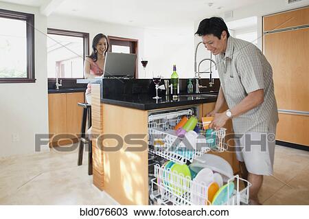Stock Image - Japanese man doing dishes while woman uses laptop. Fotosearch