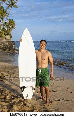 Stock Photo - Japanese man holding surfboard on beach. Fotosearch
