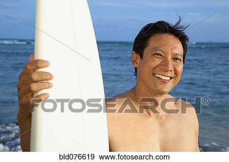 Stock Photo - Japanese man with surfboard on beach. Fotosearch