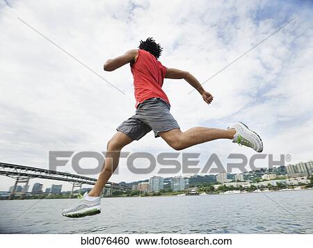 Stock Image - Mixed race man leaping next to river. Fotosearch