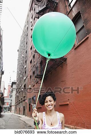Mixed race woman holding balloon on urban street View Large Photo Image Stock Image - Mixed race woman holding balloon on urban street. Fotosearch