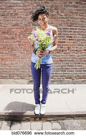Mixed race woman holding bouquet on urban sidewalk View Large Photo Image Stock Photograph - Mixed race woman holding bouquet on urban sidewalk. Fotosearch