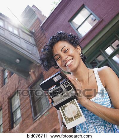 Stock Image - Mixed race woman holding instant camera. Fotosearch