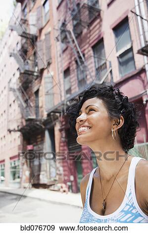 Stock Photo - Mixed race woman looking up on urban street. Fotosearch