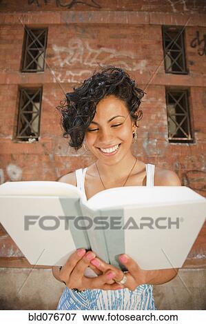 Mixed race woman reading book in front of urban building View Large Photo Image Stock Photo - Mixed race woman reading book in front of urban building. Fotosearch