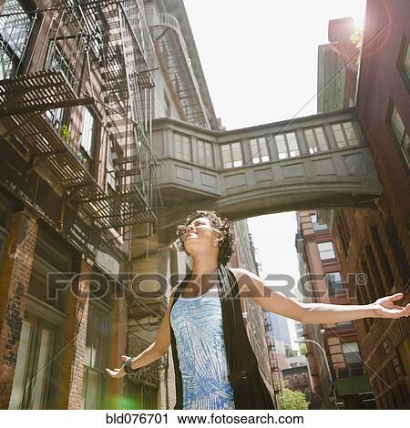 Stock Image - Mixed race woman with arms outstretched on urban street. Fotosearch