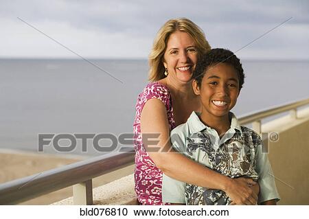 Stock Image - Woman hugging boy on balcony overlooking beach. Fotosearch