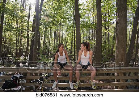 Stock Image - Women in sportswear sitting on bridge railing. Fotosearch