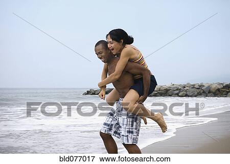 Stock Photo - African man giving girlfriend piggy back ride at beach. Fotosearch