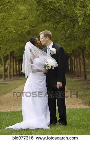 Stock Photograph - Bride and groom kissing in grass. Fotosearch
