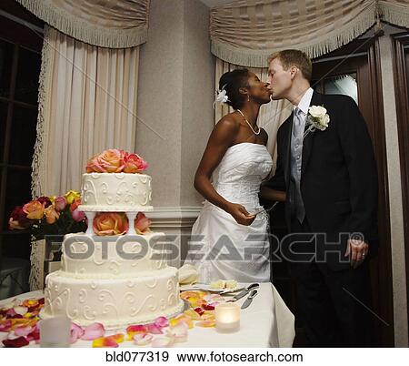 Stock Photo - Bride and groom kissing next to wedding cake. Fotosearch