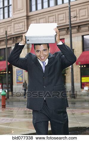 Stock Photo - Businessman covering head with briefcase in rain. Fotosearch