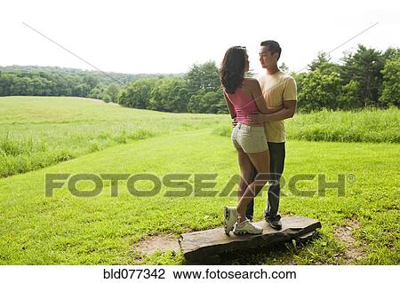 Stock Image - Hispanic couple standing on rock in field. Fotosearch
